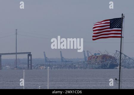 Una bandiera americana è visibile insieme ai resti del Francis Scott Key Bridge fuori Baltimora, Maryland, dopo che una nave portacontainer ha perso energia elettrica e ha colpito il ponte nelle prime ore del mattino martedì 26 marzo 2024 a Baltimora, MD, USA. Sei persone sono scomparse e presumibilmente morte dopo che una nave container ha colpito il monumento Francis Scott Key Bridge nella città americana di Baltimora. La Guardia Costiera ha detto di aver sospeso la ricerca e iniziato uno sforzo di recupero. Diversi veicoli stavano attraversando il ponte, che è lungo più di 1,6 km, quando è crollato dopo che la nave ha colpito un supporto. Dicono gli ufficiali Foto Stock