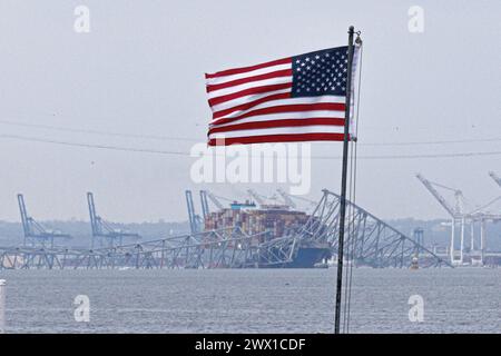 Una bandiera americana è visibile insieme ai resti del Francis Scott Key Bridge fuori Baltimora, Maryland, dopo che una nave portacontainer ha perso energia elettrica e ha colpito il ponte nelle prime ore del mattino martedì 26 marzo 2024 a Baltimora, MD, USA. Sei persone sono scomparse e presumibilmente morte dopo che una nave container ha colpito il monumento Francis Scott Key Bridge nella città americana di Baltimora. La Guardia Costiera ha detto di aver sospeso la ricerca e iniziato uno sforzo di recupero. Diversi veicoli stavano attraversando il ponte, che è lungo più di 1,6 km, quando è crollato dopo che la nave ha colpito un supporto. Dicono gli ufficiali Foto Stock