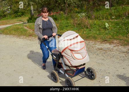 in campagna una donna spinge un passeggino con un neonato Foto Stock