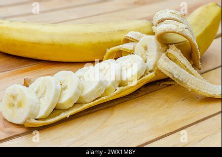 Primo piano di una banana sbucciata a metà e tagliata a segmenti, appoggiata su una superficie di legno chiaro Foto Stock