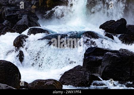 Una cascata con molte rocce sullo sfondo. L'acqua è bianca e le rocce sono nere. Foto Stock