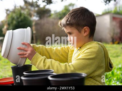 Ragazzo che piantava semi in pentole in giardino Foto Stock