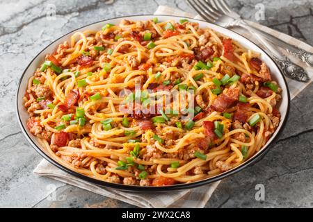 Gli spaghetti di cowboy sono realizzati con pomodori arrostiti al fuoco, manzo macinato, pancetta e formaggio cheddar in primo piano sul piatto del tavolo. Orizzontale Foto Stock
