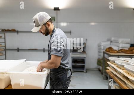 giovane fornaio maschio adulto, che controlla se l'impasto per il pane è pronto, scuola di panetteria. Foto Stock