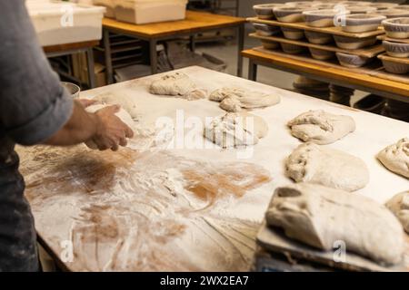 fornaio maschile non riconoscibile, preparando l'impasto per preparare il pane sul tavolo del fornaio con farina cosparsa, scuola di panetteria. Foto Stock