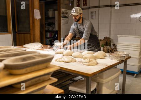 panettiere maschio giovane, prepara impasti per preparare il pane sul tavolo della panetteria, pesa gli impasti, scuola di panetteria. Foto Stock