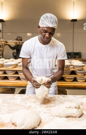 Sorridente giovane nero che lavora in una fabbrica di pane, imparando il mestiere. Foto Stock