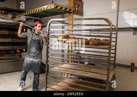 Il maestro panettiere latino prende i pani dal forno e li mette al fresco Foto Stock