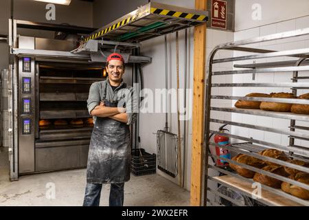 Il maestro latino baker prende i pani fuori dal forno e li mette al fresco, posa di ritratti e guarda la macchina fotografica Foto Stock