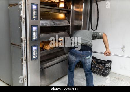 il giovane maestro panettiere latino prende i pani dal forno e li mette al fresco Foto Stock