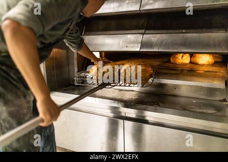 il giovane maestro panettiere latino prende i pani dal forno e li mette al fresco Foto Stock