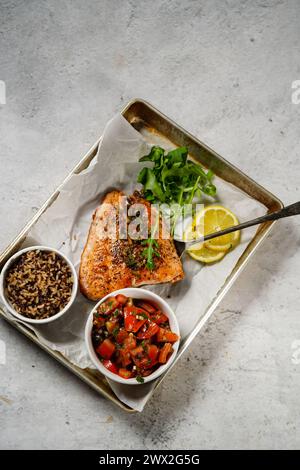 Filetto di salmone al forno servito con insalata di pomodoro, riso quinoa e rucola su un vassoio da forno Foto Stock