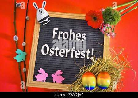 27 marzo 2024: Saluti: Buona Pasqua testo su tavola circondato da decorazioni pasquali su sfondo rosso. FOTOMONTAGGIO *** Gruß: Frohes Osterfest Text auf einer Tafel umgeben von Osterdekoration auf rotem Hintergrund. FOTOMONTAGE Foto Stock