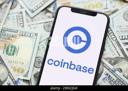 KIEV, UCRAINA - 15 MARZO 2024 logo Coinbase sullo schermo dell'iPhone con molte banconote da cento dollari. Portale di scambio di criptovalute Foto Stock