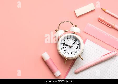 Vista dall'alto della sveglia bianca e delle forniture scolastiche con spazio per copiare il testo su sfondo rosa. Ritorno al concetto di scuola Foto Stock