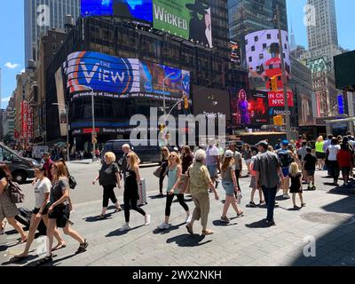 Una folla di persone attraversa la strada nel cuore di New York City Times Square, circondato da cartelloni e pubblicità Foto Stock