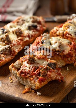 Pane per pizza fatto con salsiccia, mozzarella e pomodoro sause tagliato su un vecchio tagliere di legno Foto Stock