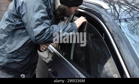 Maschio ladro burglar passando da sciocchi attraverso la crepa nella finestra di parcheggio auto vuoto, egli apre la porta sbloccata, tira denaro in contanti o smartphone o portafoglio, Foto Stock