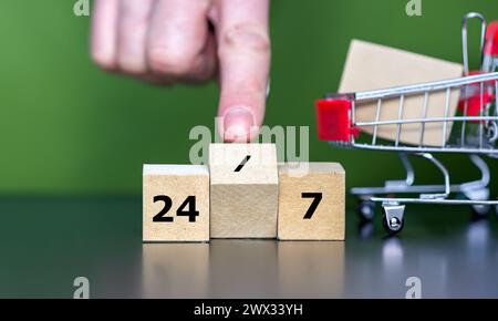 I cubi di legno formano l'espressione "24 7" accanto a un carrello della spesa. Simbolo di un negozio aperto 24 ore su 24, 7 giorni su 7. Foto Stock