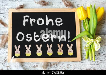 27 marzo 2024: Auguri di Pasqua per Pasqua, su un tavolo su un rustico tavolo bianco con tulipani gialli. FOTOMONTAGGIO *** Frohe Ostern Gruß zu Ostern, auf einer Tafel auf einem rustikalen Weißen Tisch zusammen mit gelben Tulpen. FOTOMONTAGE Foto Stock