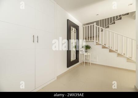 Corridoio di una casa unifamiliare a più piani con armadi incorporati, scale con ringhiere in metallo e pavimenti in gres color crema Foto Stock