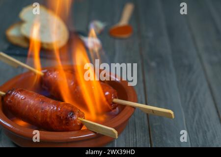 Tipica tapa spagnola, chorizo al fuoco in una casseruola di terracotta con fette di pane sullo sfondo Foto Stock