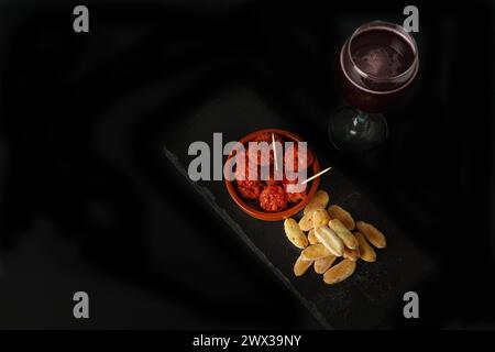 Vista dall'alto di una casseruola in terracotta con salsiccia fritta, pane e un bicchiere di vino isolato su sfondo nero Foto Stock