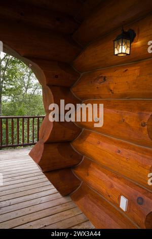 Casa in legno scandinavo con tinto rossastro marrone, con arco e parete realizzati con grandi tronchi a fessura e veranda in legno grigio in estate, Quebec, Canada Foto Stock