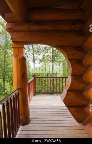 Casa in legno scandinavo con tinto rossastro marrone, con arco e muro di grandi tronchi a fessura e veranda in legno in estate, Quebec, Canada Foto Stock