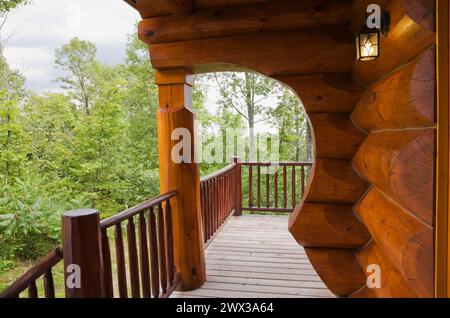 Casa in legno scandinavo con tinto rossastro marrone, con arco e parete realizzati con grandi tronchi a fessura e veranda in legno grigio in estate, Quebec Foto Stock