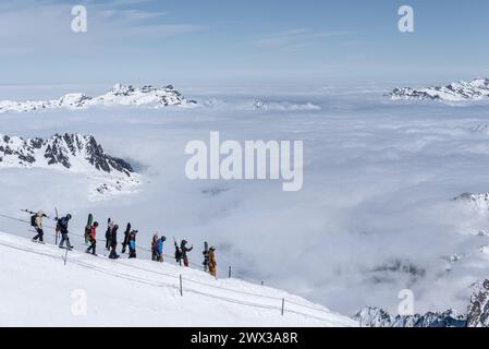 Chamonix, Francia - 4 marzo 2024: Un gruppo di 8 snowboarder e sciatori che camminano lungo la pista sulla cresta da Aiguille du Midi alla Vallee Blanche Foto Stock