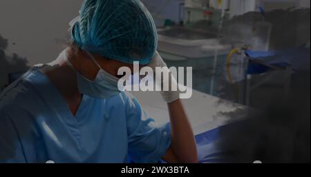 Immagine di nuvole nere sopra triste infermiera birazziale femminile con maschera facciale in ospedale. settimana di consapevolezza della salute mentale e concetto di celebrazione generi digitali Foto Stock