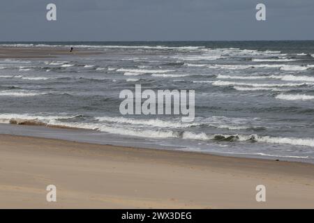 Onde con creste bianche inondare la spiaggia sabbiosa Foto Stock