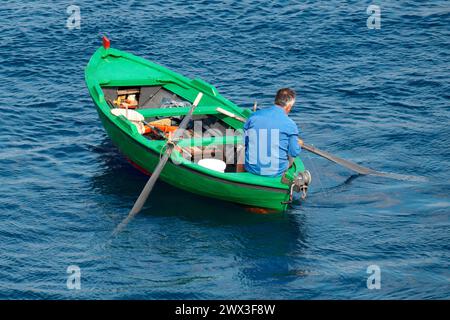 Un uomo su una barca a remi che pesca senza canna da pesca e galleggiante ma con lenze a mano Bari, Puglia, Italia Foto Stock