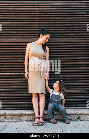 donna incinta e figlio che si guardano felici seduti su sfondo a righe Foto Stock