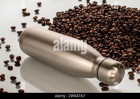 Una bottiglia in metallo thermos sul tavolo con fragranti chicchi di caffè tostati, macro. Foto Stock