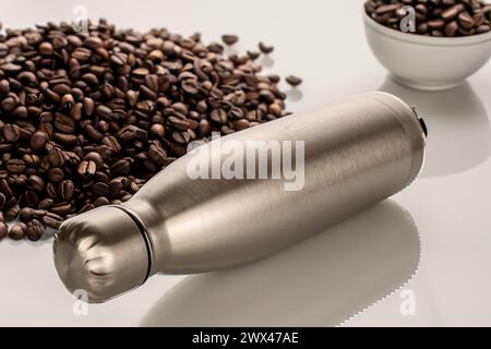 Una bottiglia in metallo thermos sul tavolo con fragranti chicchi di caffè tostati, macro. Foto Stock