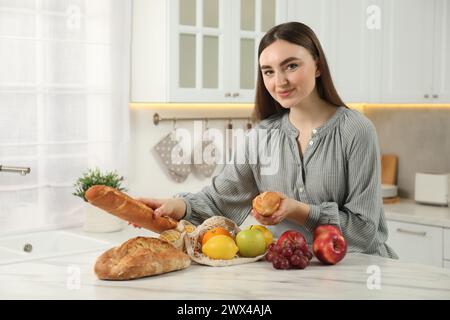 Donna con baguette e sacchetto di frutta fresca al tavolo di marmo chiaro in cucina Foto Stock