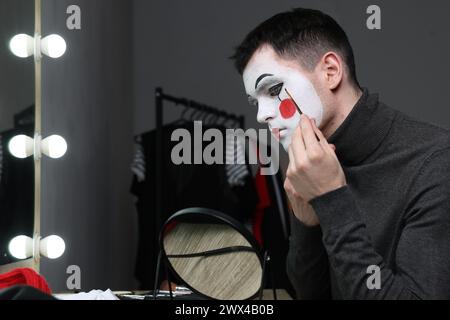 Giovane che applica il trucco mimo vicino allo specchio nello spogliatoio Foto Stock