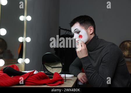 Giovane che applica il trucco mimo vicino allo specchio nello spogliatoio Foto Stock