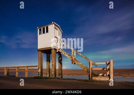 Una vista notturna al chiaro di luna con un cielo limpido e l'aurora boreale del rifugio sulla strada rialzata di Lindisfarne nel Northumberland Foto Stock