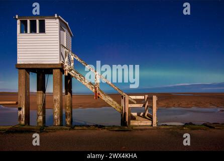 Una vista notturna al chiaro di luna con un cielo limpido e l'aurora boreale del rifugio sulla strada rialzata di Lindisfarne nel Northumberland Foto Stock