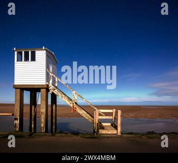 Una vista notturna al chiaro di luna con un cielo limpido e l'aurora boreale del rifugio sulla strada rialzata di Lindisfarne nel Northumberland Foto Stock