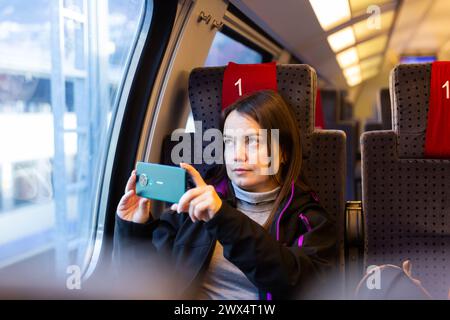 Il viaggiatore interessato filma paesaggi dietro il vetro in treno espresso Foto Stock