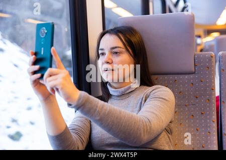 Il viaggiatore interessato filma paesaggi dietro il vetro in treno espresso Foto Stock