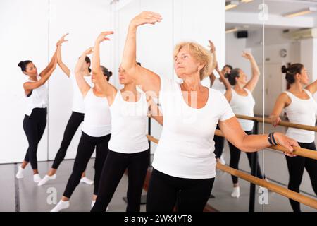 Varie donne anziane che esercitano il balletto si muove con il formatore Foto Stock