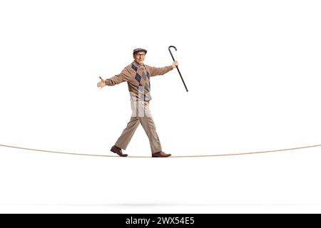 Foto a tutta lunghezza di un anziano gentiluomo che tiene in mano un bastone e cammina su una corda isolata su sfondo bianco Foto Stock