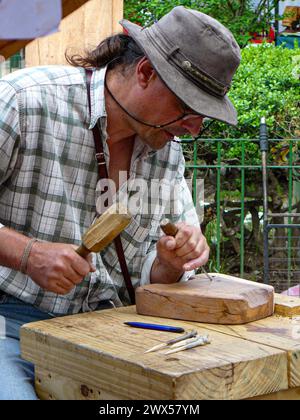 uomo che intaglia un pezzo di legno a una fiera dell'artigianato di strada Foto Stock