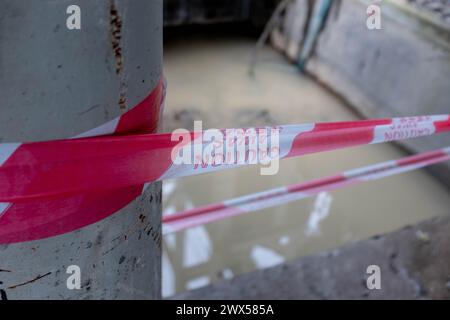 Un nastro di plastica di avvertenza avvolto intorno a una pericolosa cabina di sollevamento riempita di acqua sporca in un cantiere Foto Stock