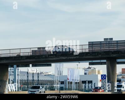 Strasburgo, Francia - 20 marzo 2024: Una piccola auto attraversa un ponte francese nella città di Strasburgo, con più concessionarie di auto visibili sullo sfondo, che illustrano il panorama automobilistico urbano Foto Stock